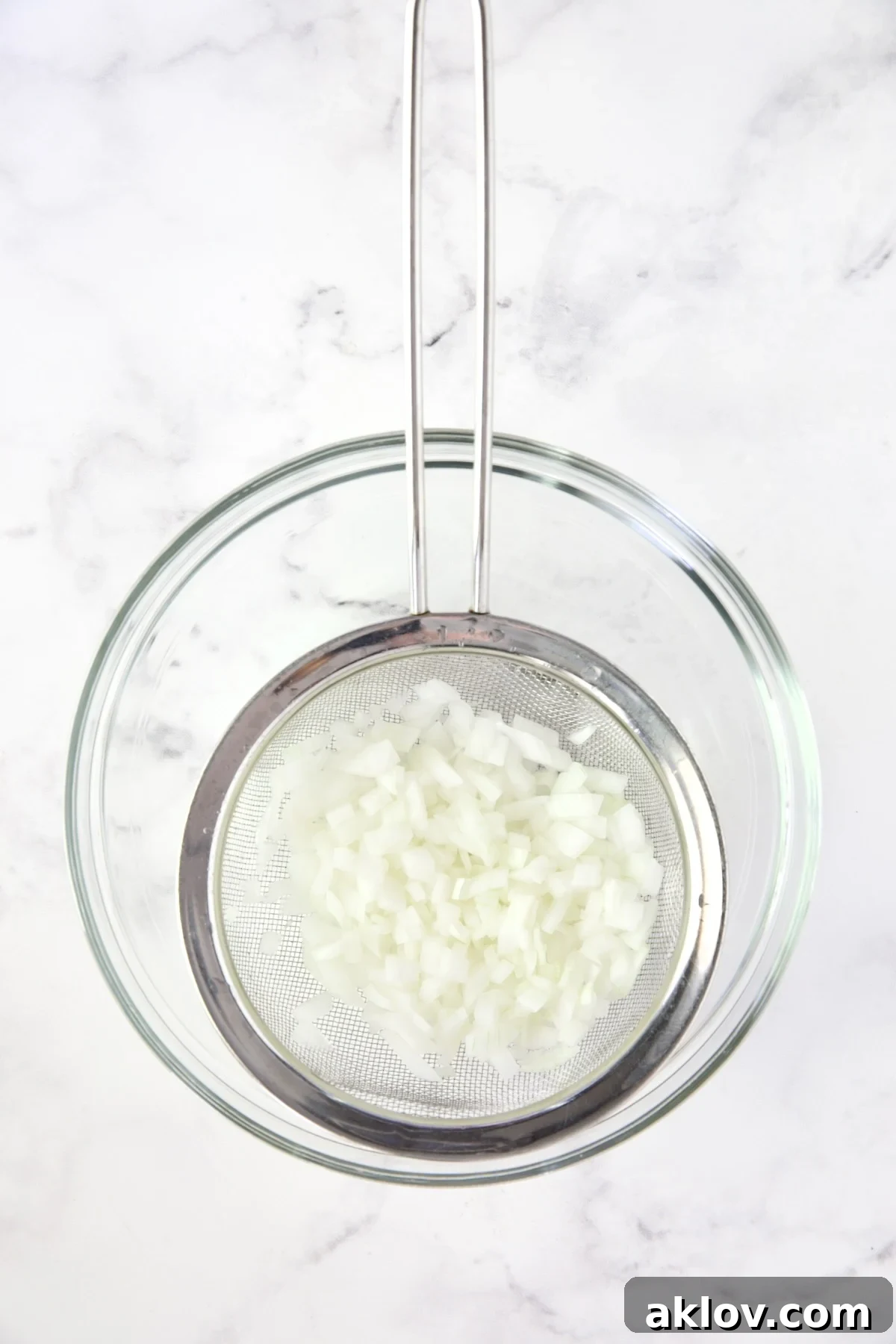 Finely diced onions in a sieve, placed over a glass bowl to drain after rinsing.