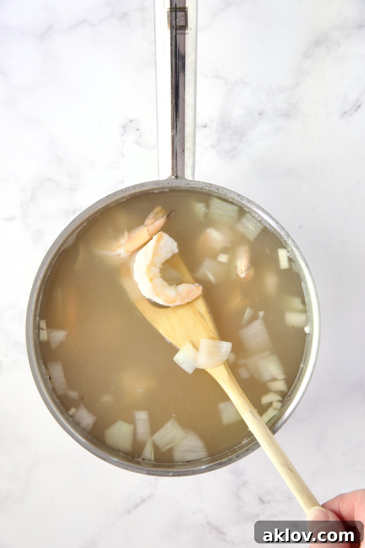Cooked shrimp in hot water with onions in stainless steel saucepan.