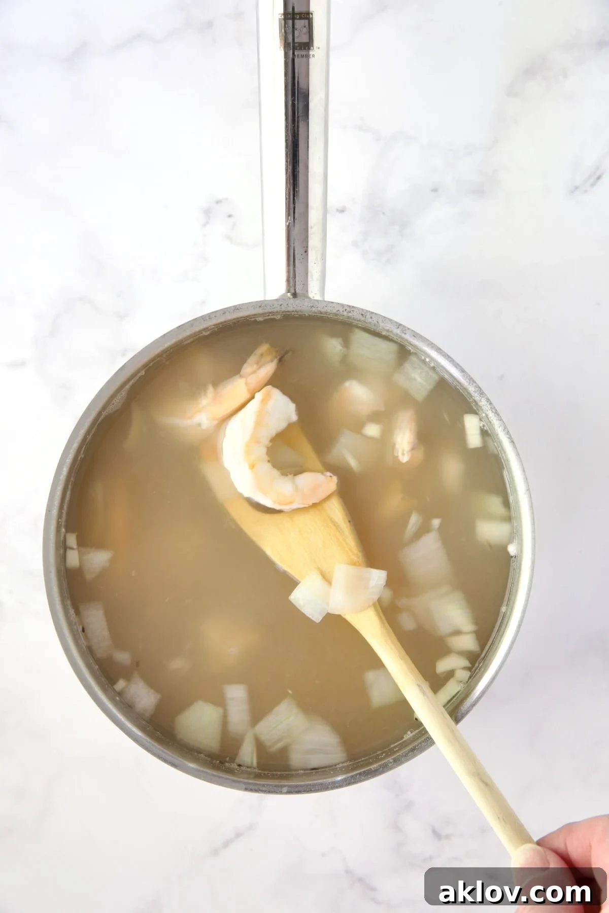 Cooked shrimp, perfectly pink, alongside onion chunks in hot water within a stainless steel saucepan.