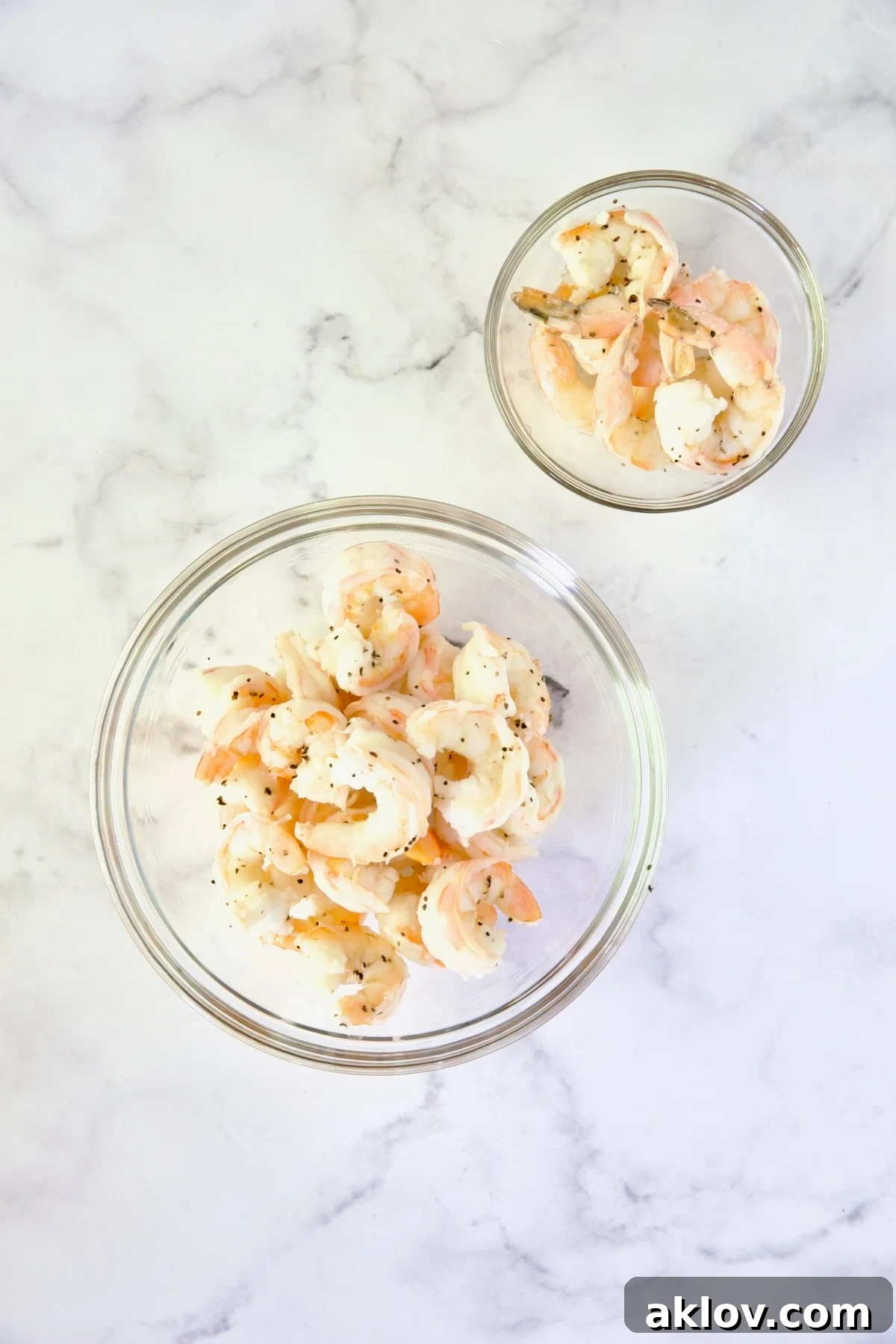 Two bowls of cooked shrimp: one with tails removed for the cocktail mix, and another with tails intact for garnish.