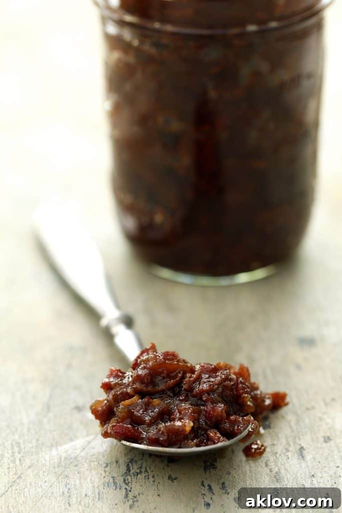 Close-up photo of bacon jam on spoon with glass jar of jam in the background.
