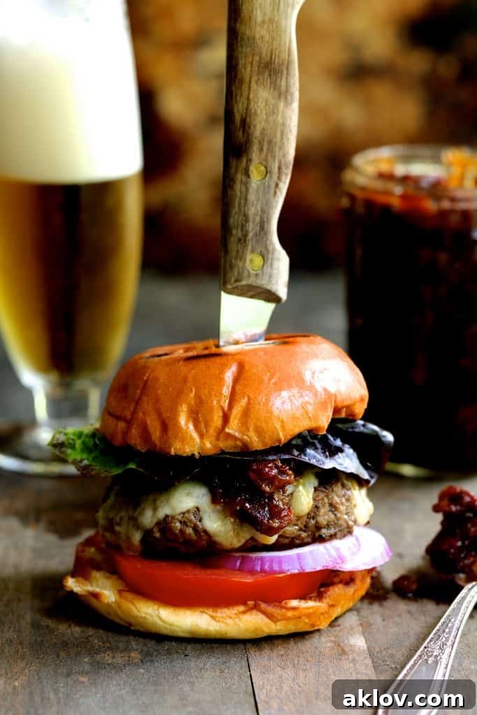 Photo of Grilled Burgers with Bacon Tomato Jam and Smoked Gouda with foamy beer in the background.