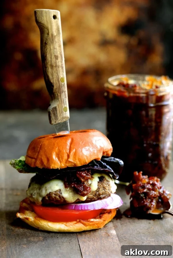 Grilled Burgers with Bacon Tomato Jam and Smoked Gouda with a steak knife through the burger and the jar of jam.