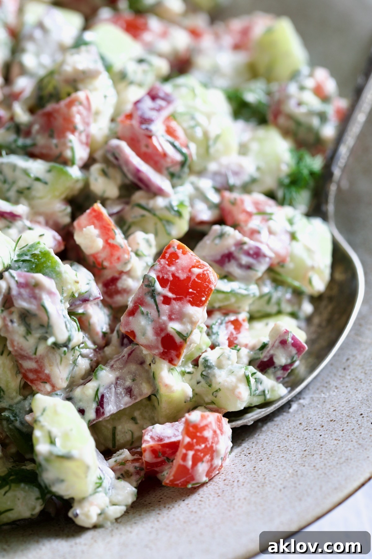 A closer view of the Creamy Cucumber Feta Tomato Salad, beautifully showcasing its vibrant colors, fresh ingredients, and the creamy texture of the dressing, with a serving spoon nestled within the bowl.