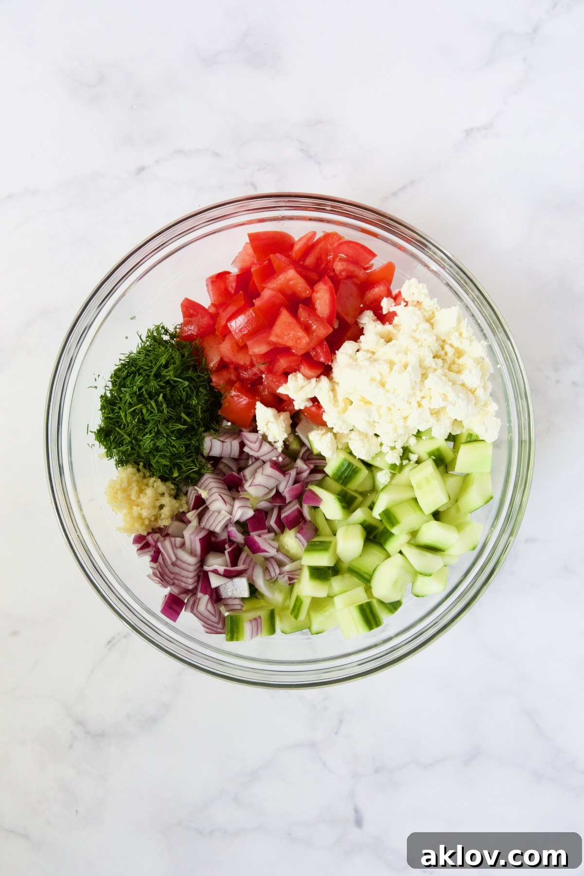 Prepped ingredients for Creamy Cucumber Feta Tomato Salad, including chopped vegetables, feta, and herbs, arranged in a large glass bowl before the dressing is incorporated.