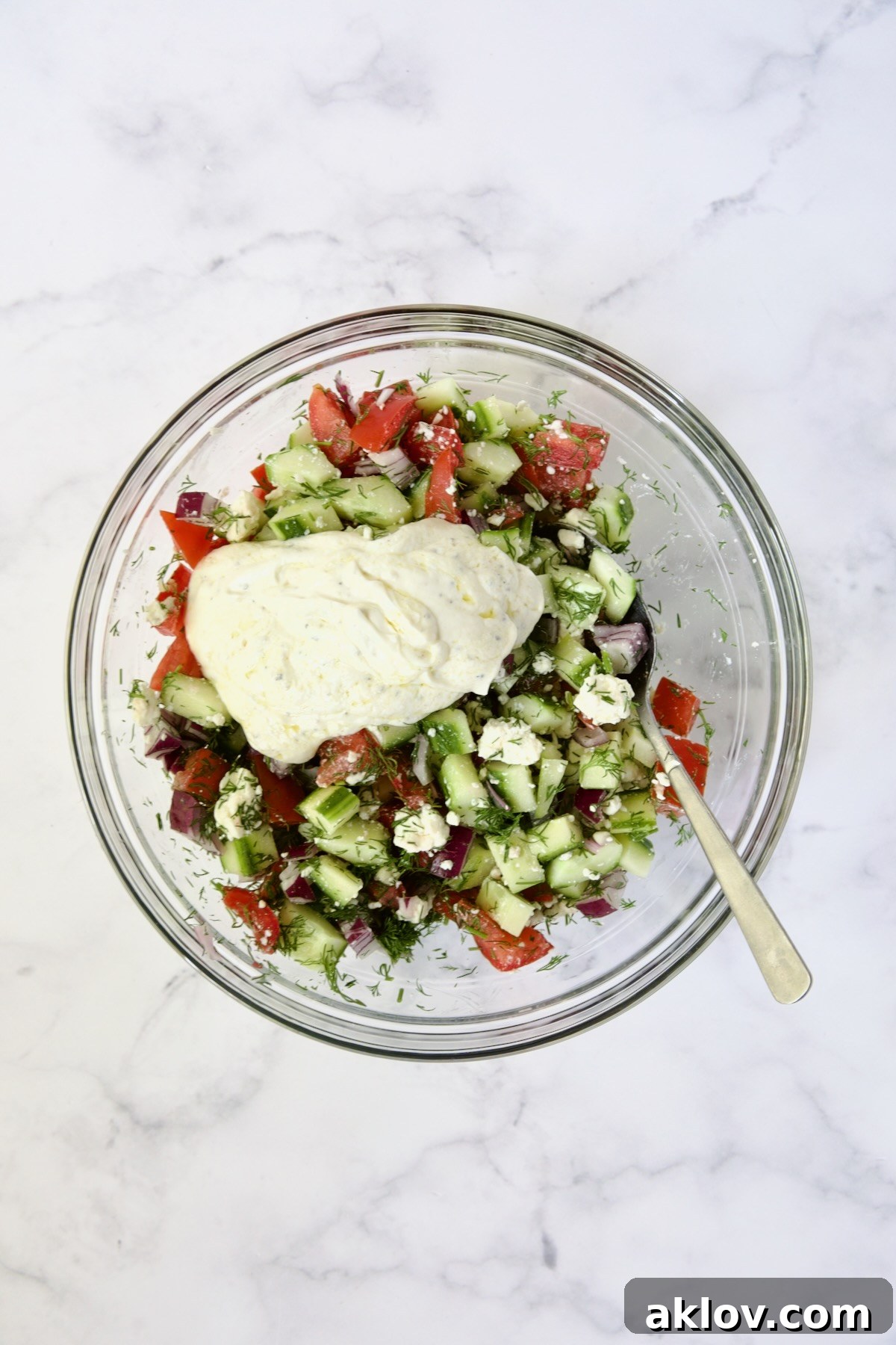 Creamy Cucumber Feta Tomato Salad with the Greek yogurt and dill dressing freshly added, awaiting the final toss and mixing.