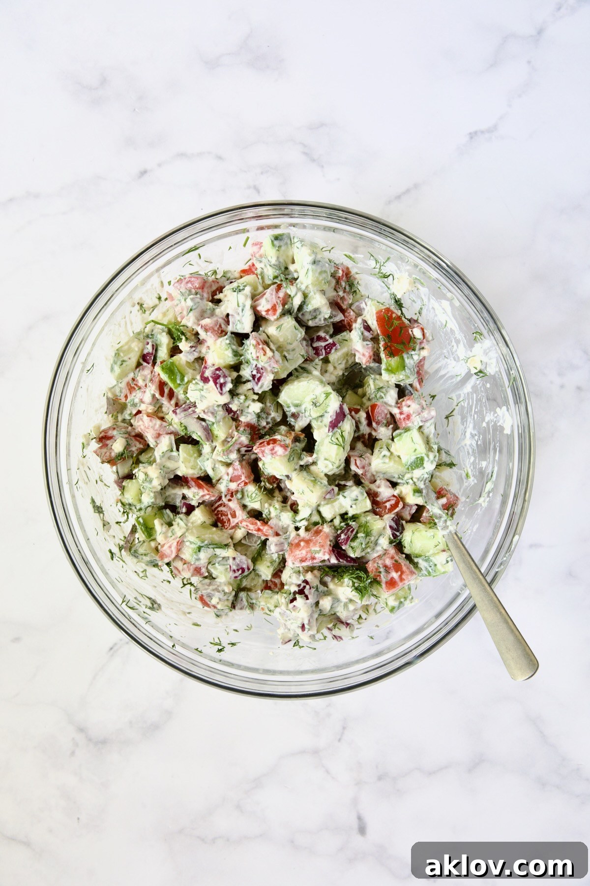 The Creamy Cucumber Feta Tomato Salad fully mixed, showcasing its vibrant ingredients and creamy dressing, presented in a clean glass bowl ready for serving.