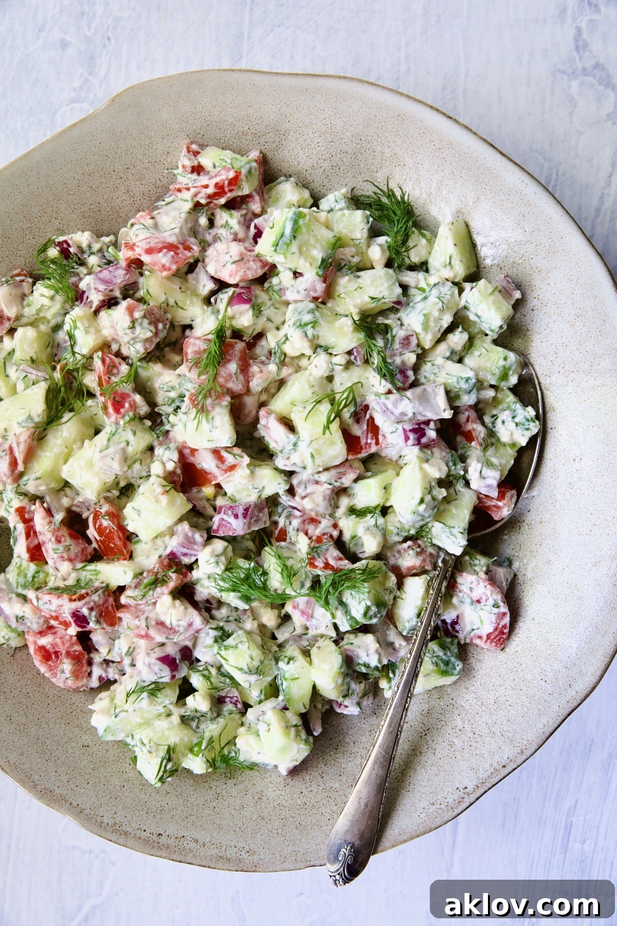 The ultimate presentation of Creamy Cucumber Feta Tomato Salad, glistening with dressing in a beautiful salad bowl with a serving spoon, inviting immediate enjoyment.