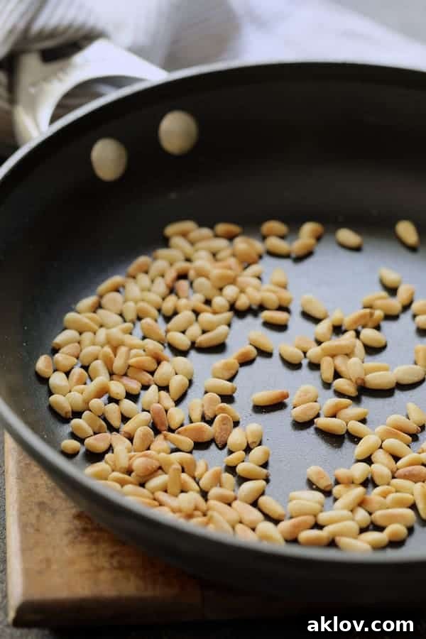 Photo of lightly toasted pine nuts in a nonstick skillet, gently browning to release their aromatic flavor.