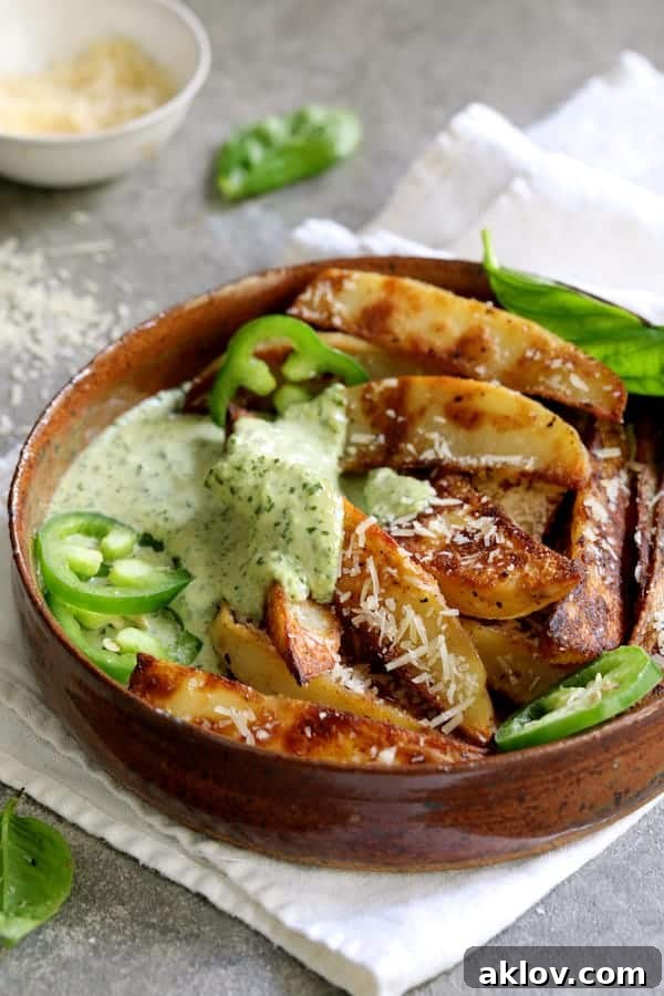 Photo of an individual serving of golden oven fries generously topped with spicy pesto aioli, garnished with fresh jalapeño slices and basil.
