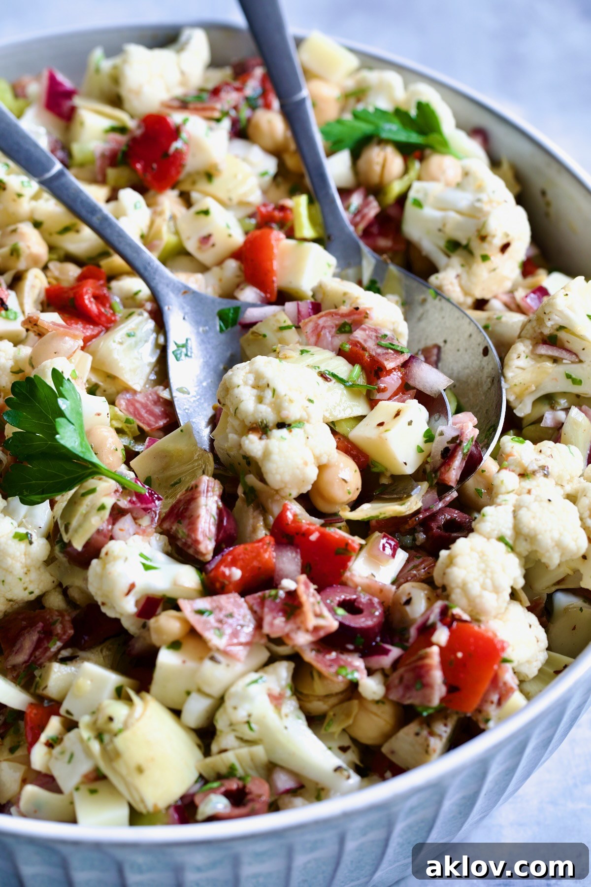 Beautifully arranged Cauliflower Antipasto Salad in a blue serving bowl, adorned with fresh parsley and serving utensils, ready to be enjoyed.