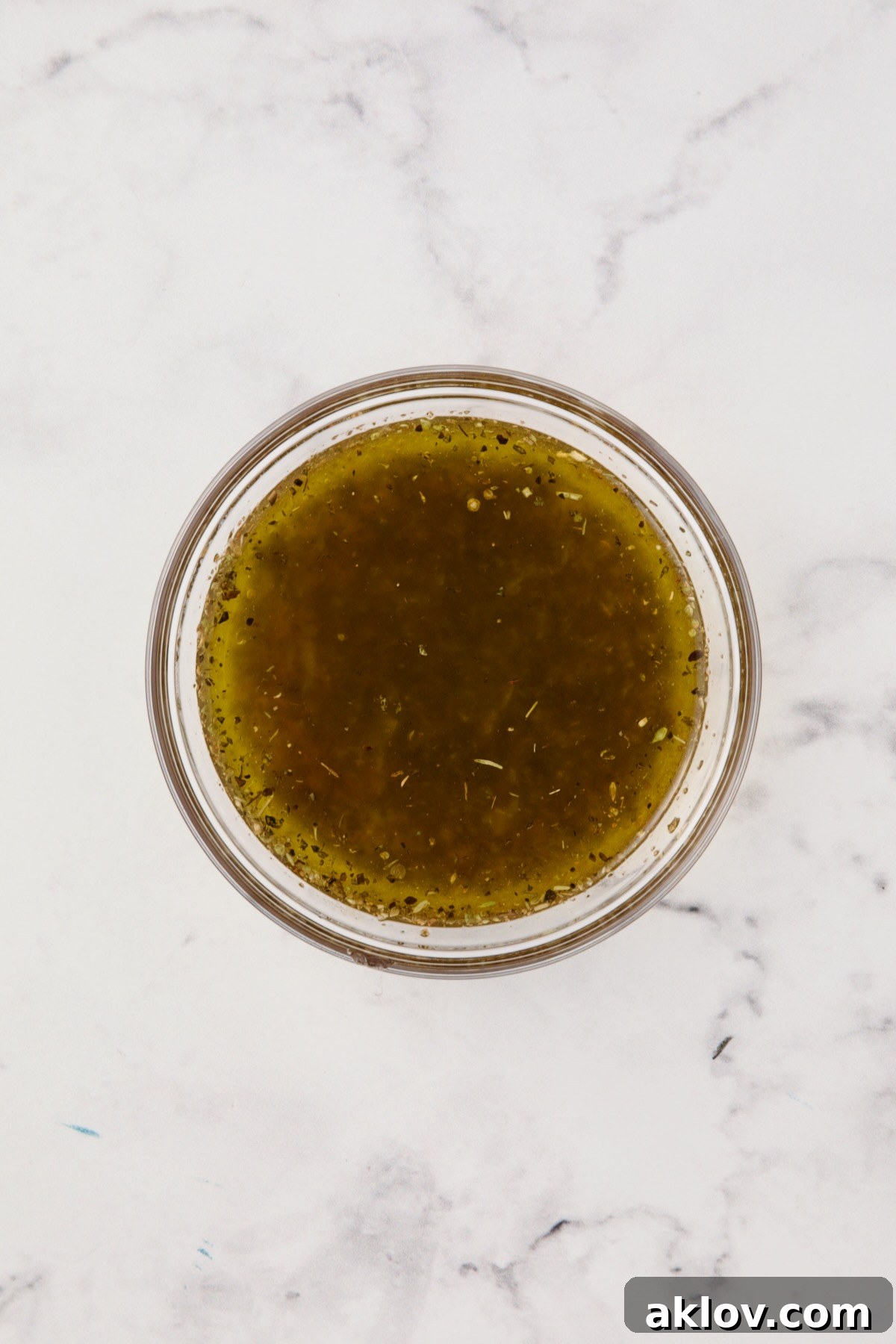 A small glass bowl containing the freshly whisked salad dressing for Cauliflower Antipasto Salad, showcasing its vibrant color and smooth texture.