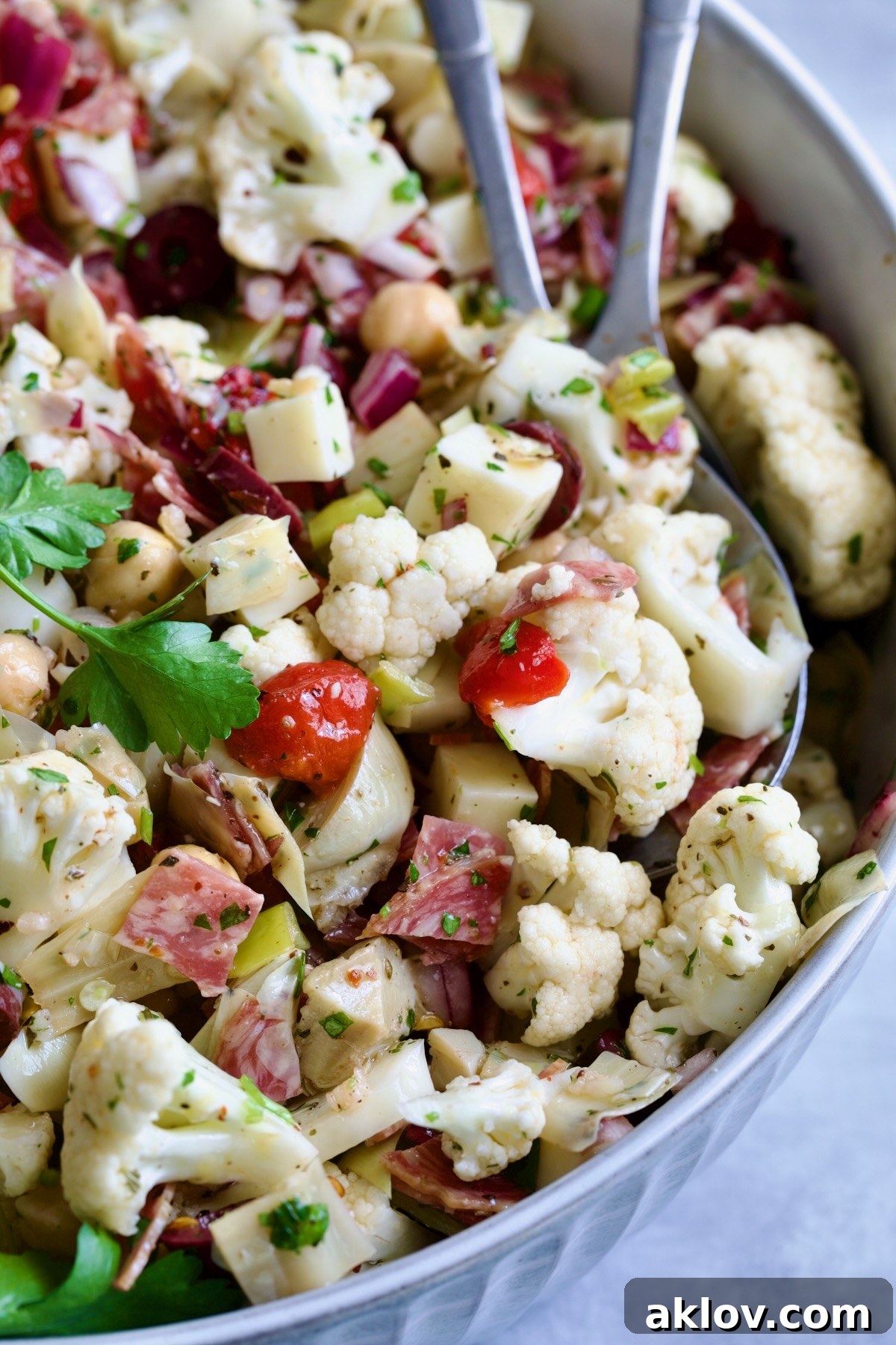 An appetizing close-up of Cauliflower Antipasto Salad, beautifully plated in a blue serving bowl with elegant serving utensils, showcasing its fresh ingredients and inviting textures.