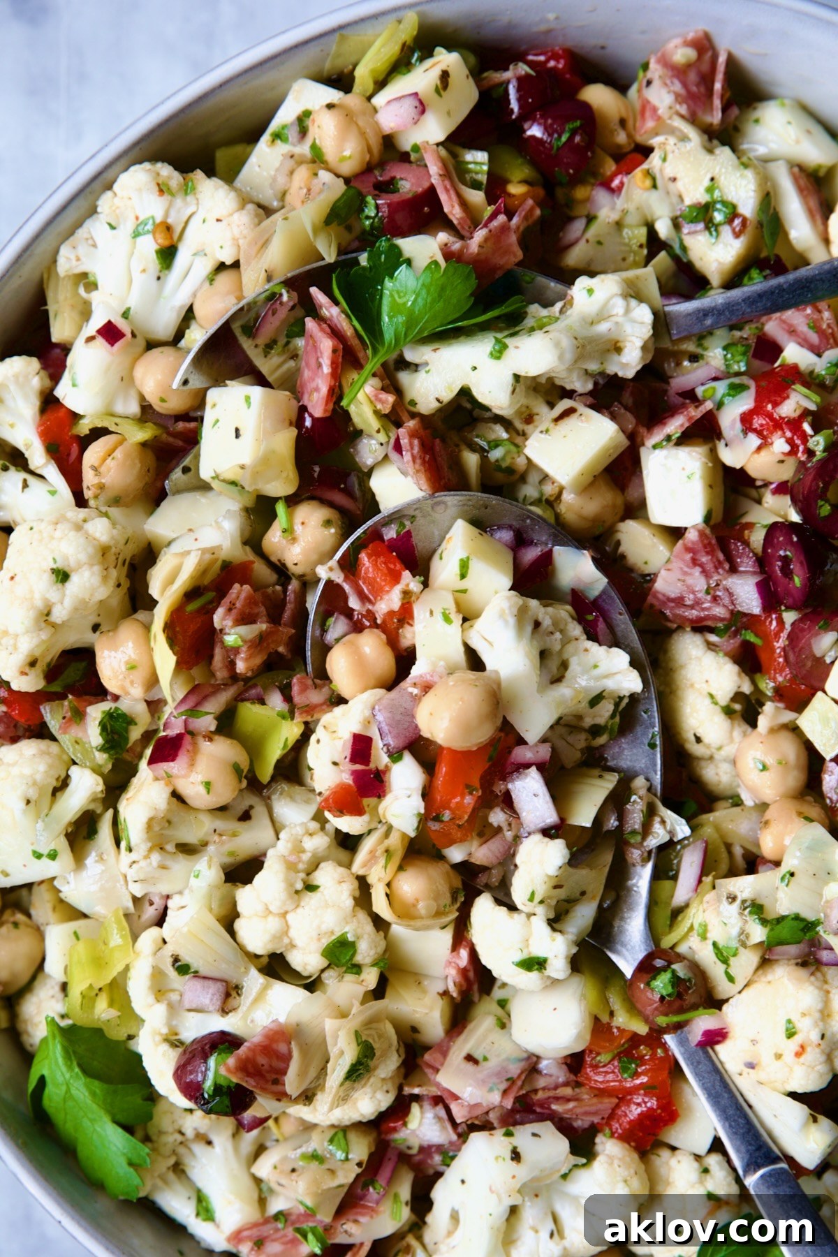 A stunning shot of Cauliflower Antipasto Salad presented in a beautiful serving bowl, with serving utensils, ready to be enjoyed as a refreshing and savory dish.