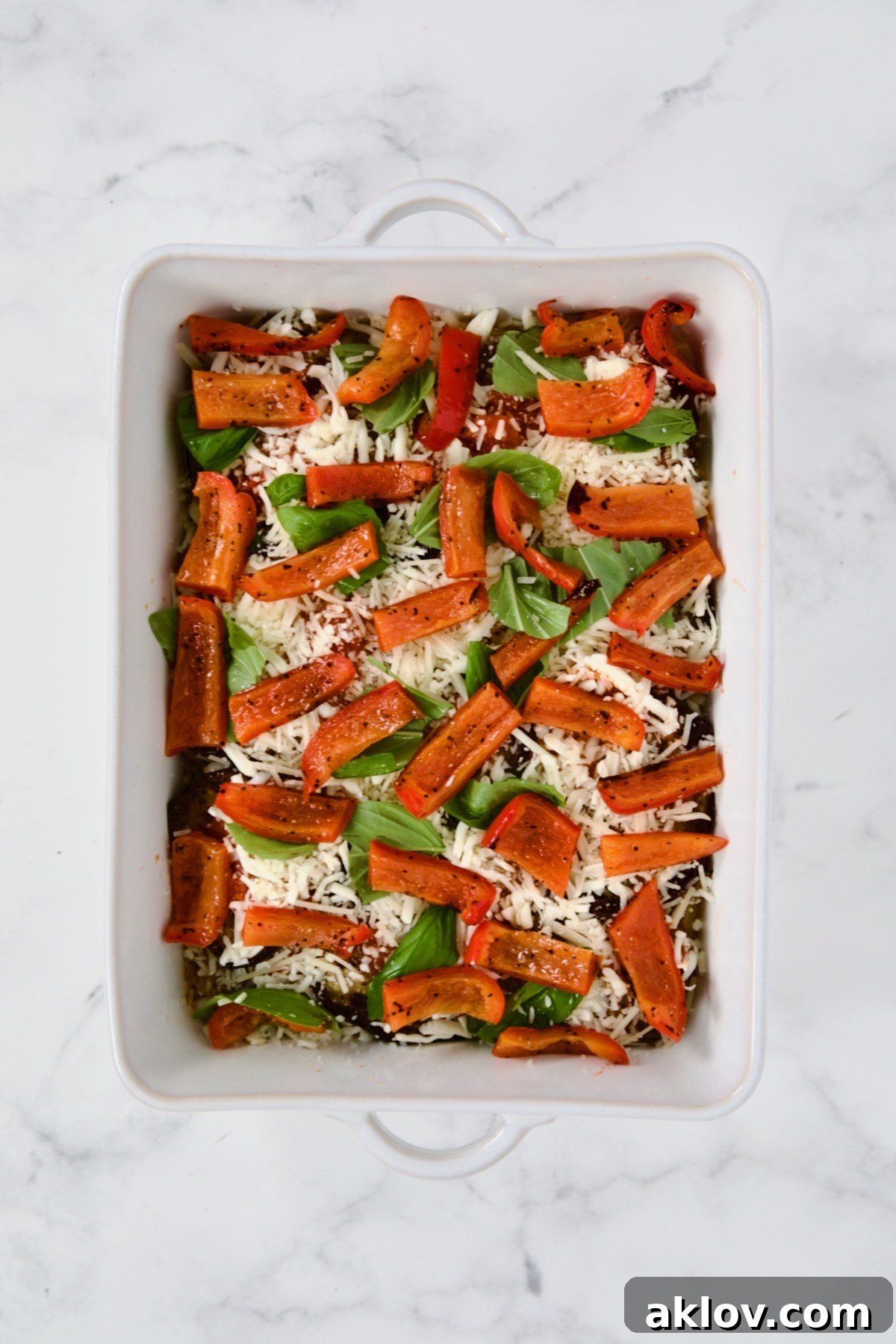 A rich layer of grilled red bell pepper strips, adding color and flavor, placed over sauce and cheese in a white rectangular baking dish for the Summer Vegetable Parmigiana.