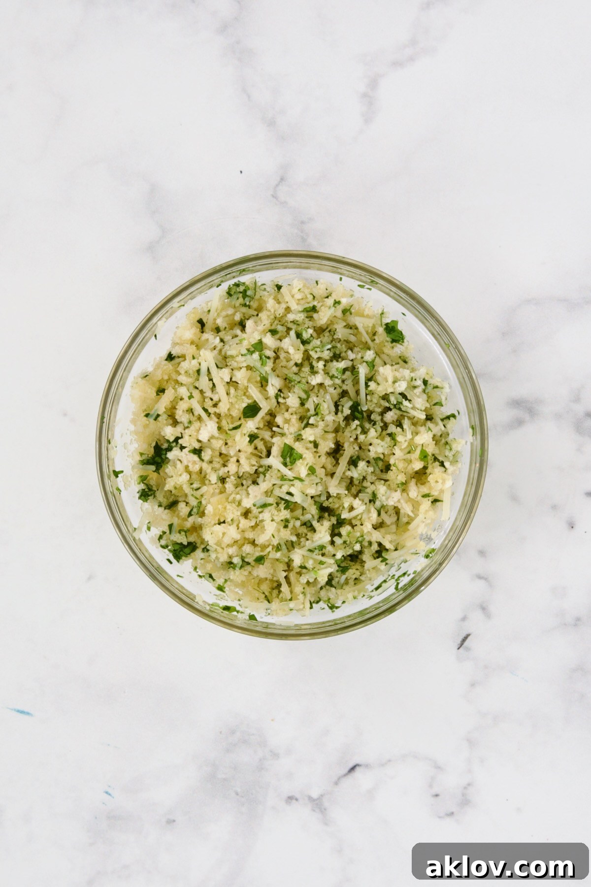 A close-up shot of panko breadcrumbs, grated Parmesan cheese, and fresh chopped parsley perfectly combined in a clear glass bowl, ready to be sprinkled as a crispy topping.