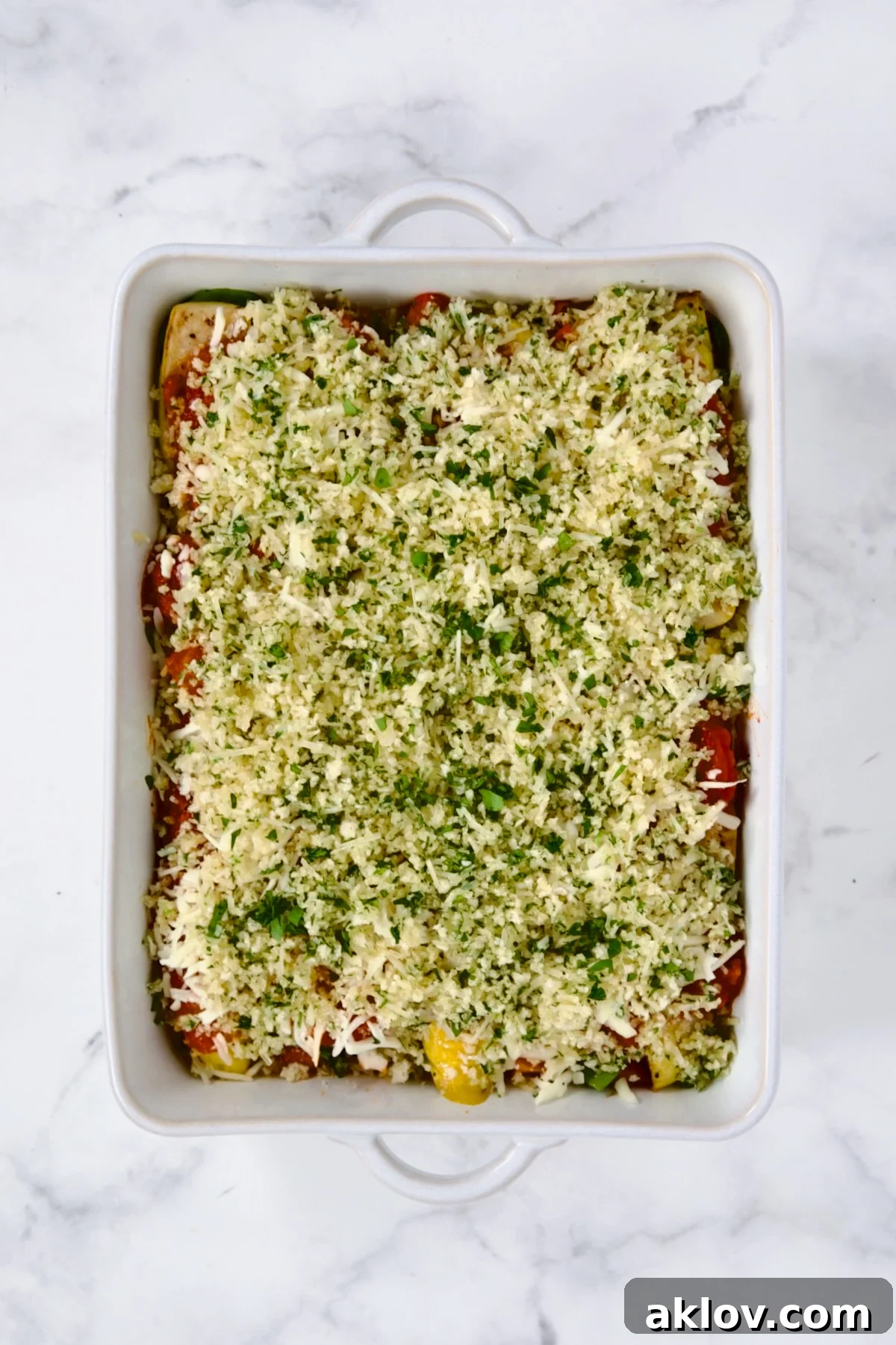 A fully assembled Summer Vegetable Parmigiana in a white rectangular baking dish, topped with panko breadcrumbs and cheese, glistening and ready for the oven.