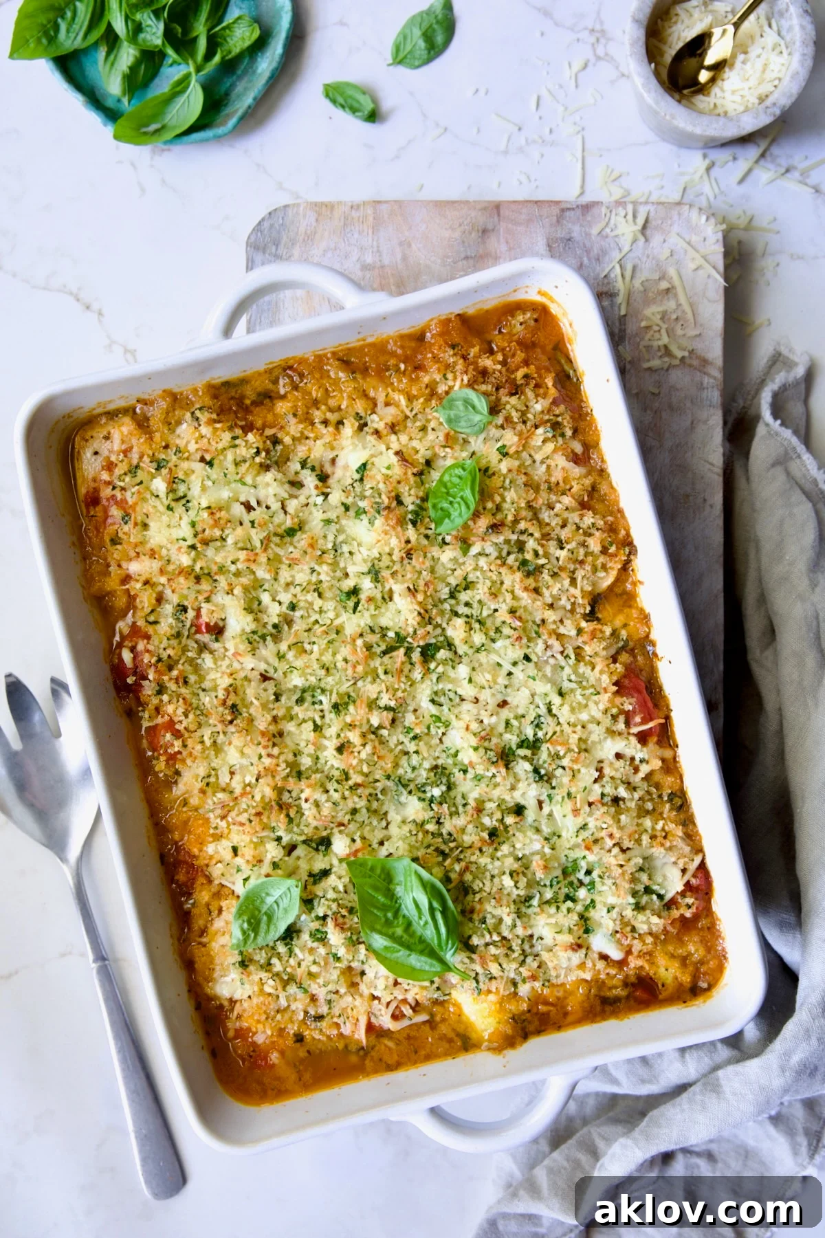 A freshly baked Summer Vegetable Parmigiana in a white rectangular baking dish, garnished with vibrant fresh basil leaves, showcasing its golden-brown topping and rich, bubbly interior.