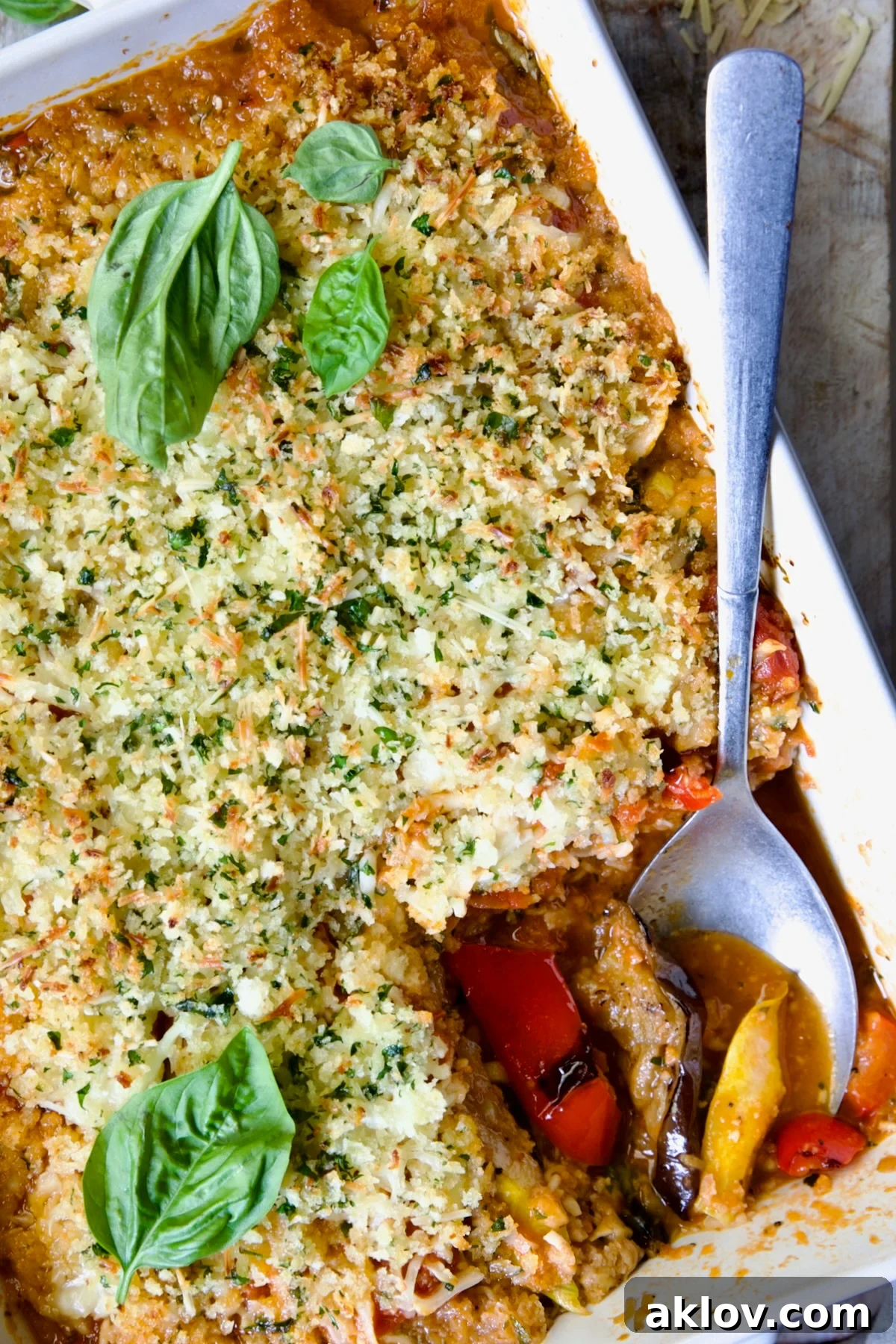 A close-up of a serving of Summer Vegetable Parmigiana in a white baking dish, showing the delicious layers of vegetables and melted cheese being scooped out with a spoon.