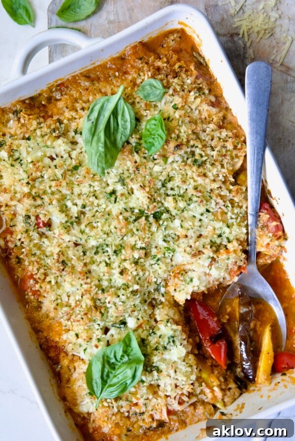 Summer Vegetable Parmigiana in a white baking dish with a serving spoon scooping some up, showcasing its golden-brown topping and rich layers.