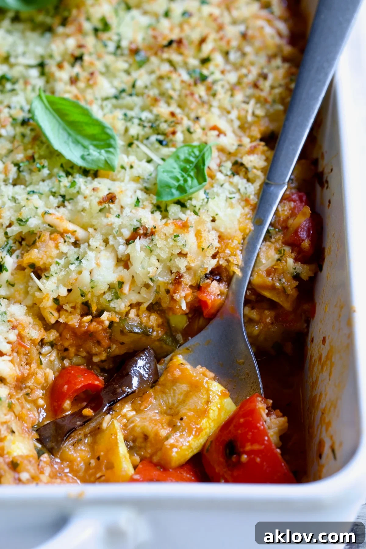 A pristine white rectangular baking dish showcasing a generous serving of Summer Vegetable Parmigiana, with golden-brown cheese and perfectly cooked vegetable layers visible, ready to be enjoyed.