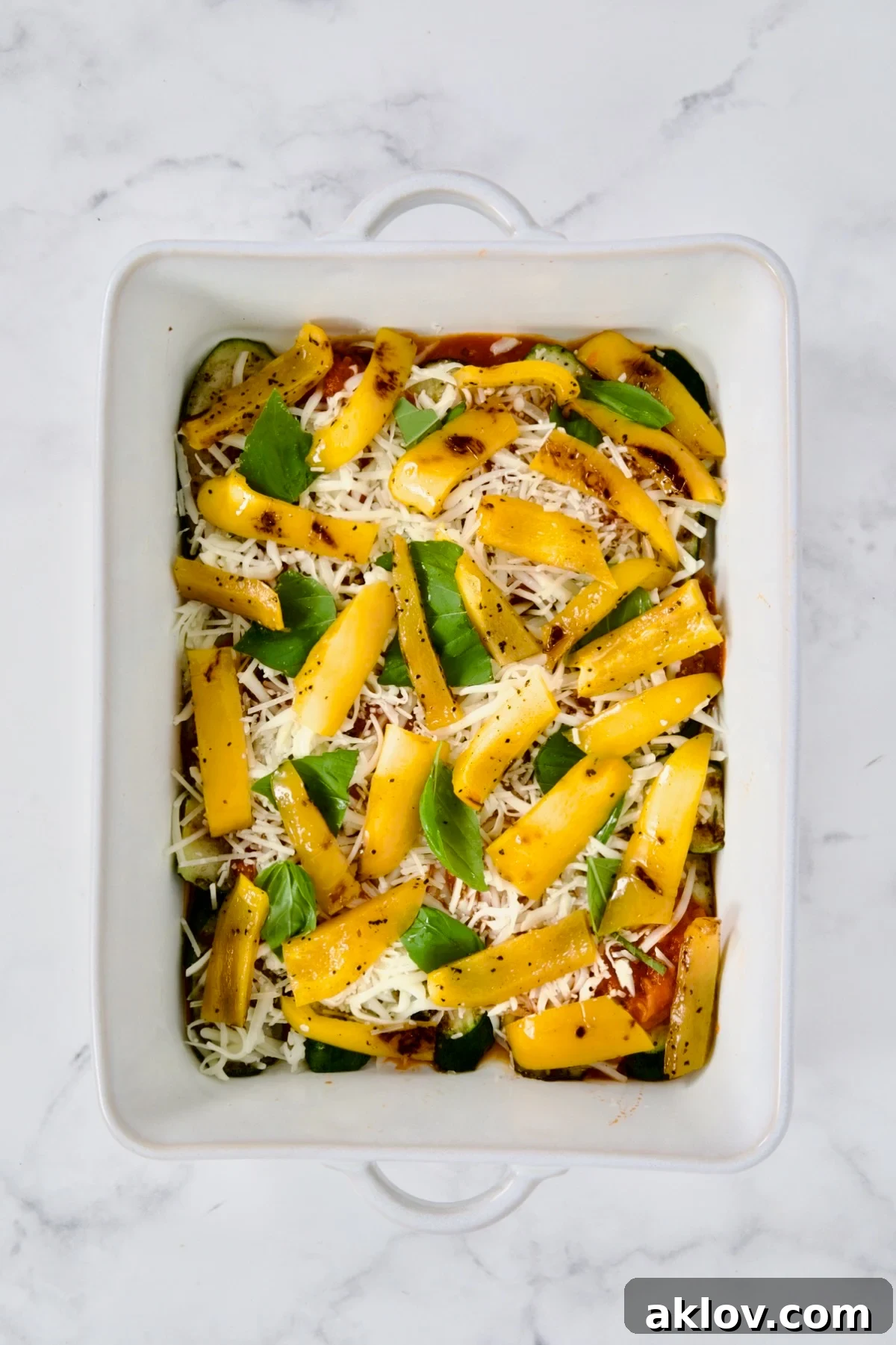 A vibrant layer of grilled yellow bell pepper strips arranged over sauce and cheese in a white rectangular baking dish, forming a colorful addition to the vegetable parmigiana layers.