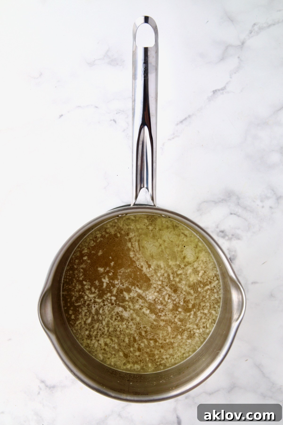 Boiling chicken broth and butter in stainless steel saucepan.