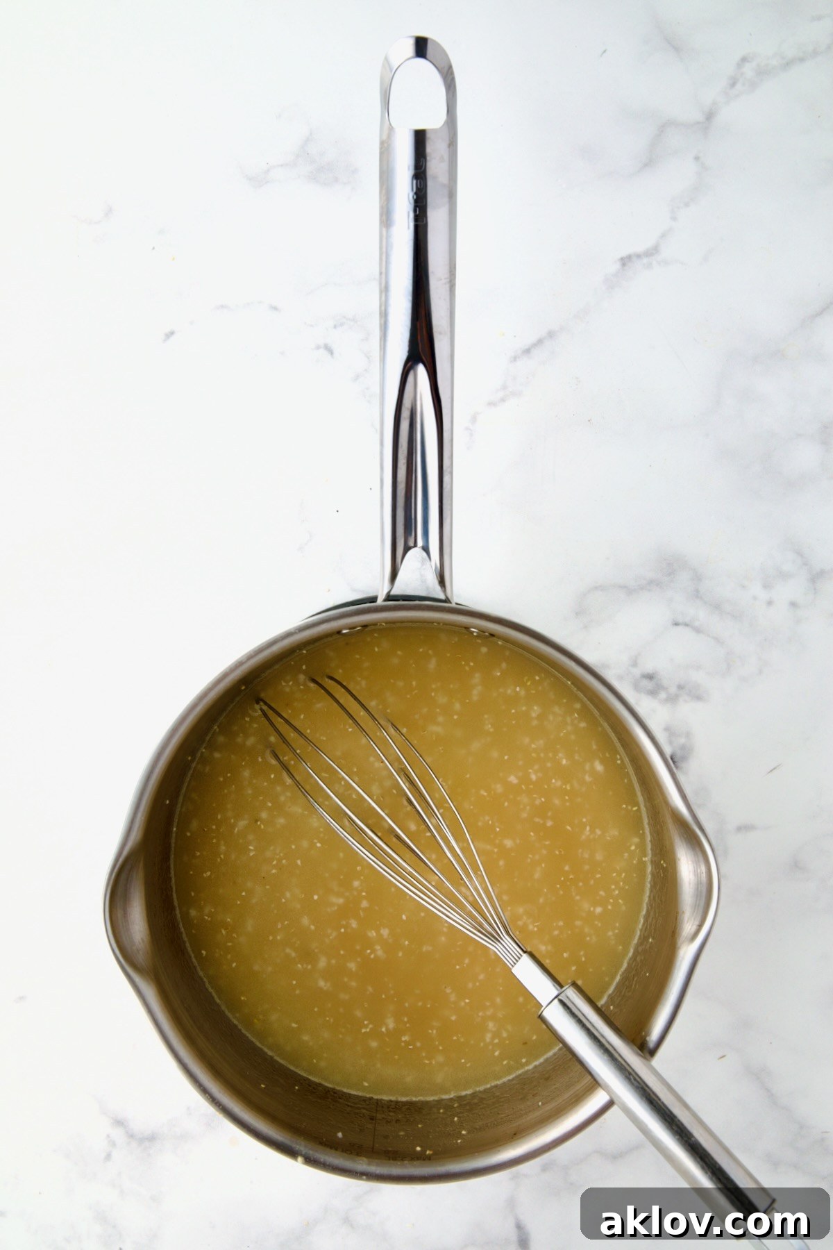 Polenta added to chicken broth in stainless steel saucepan with wire whisk.