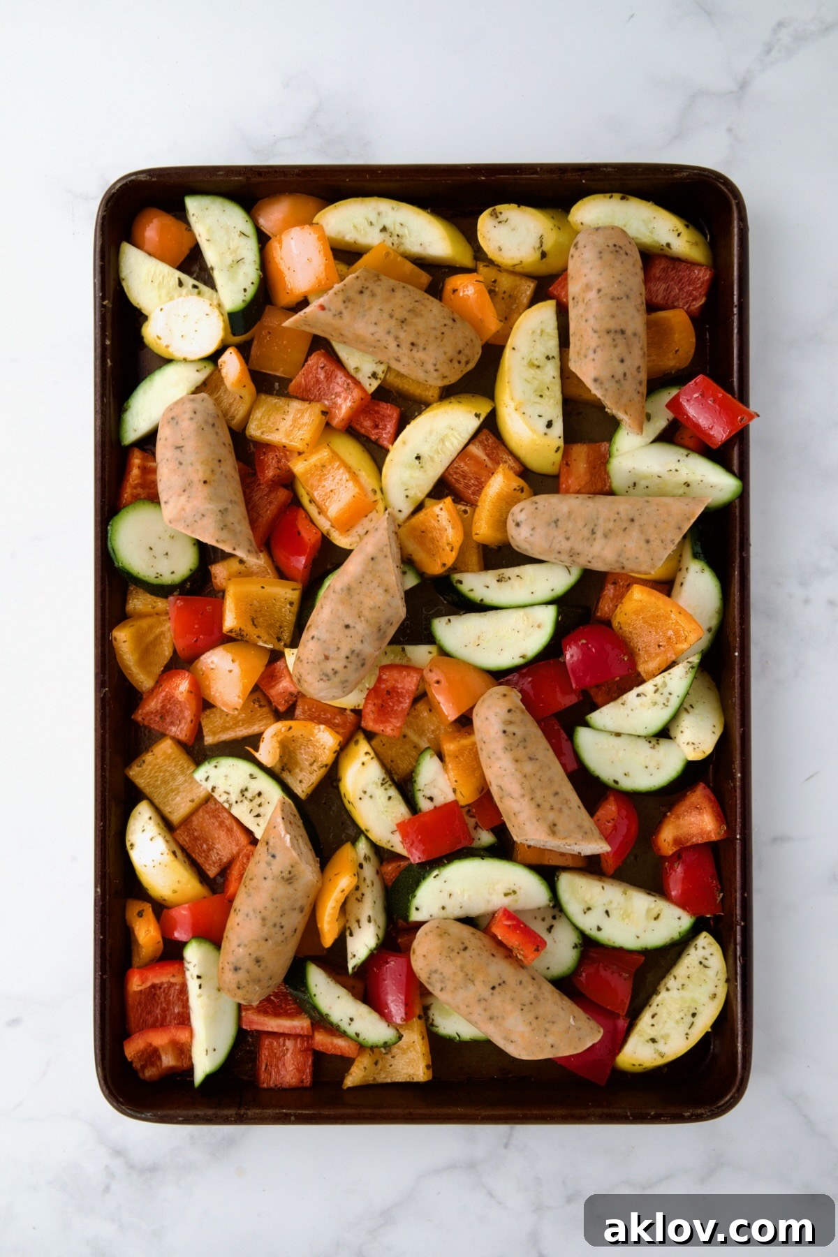 Uncooked chicken sausage and vegetables on rimmed sheet pan.