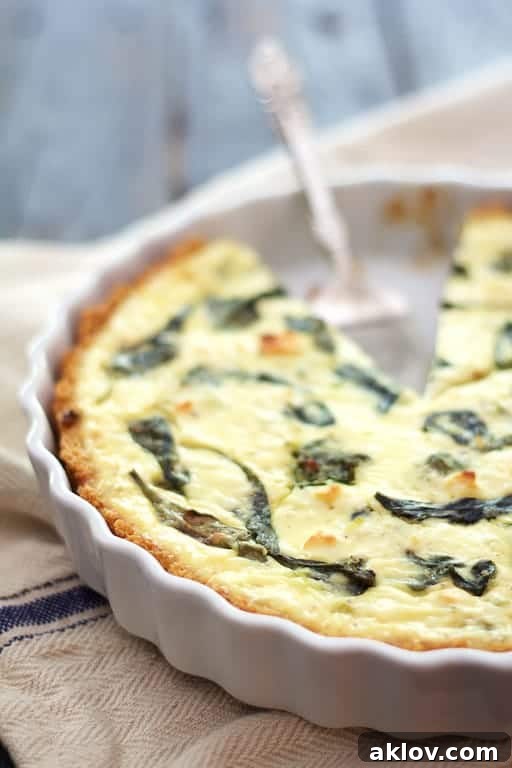 Photo of Spinach and Feta Quiche with Quinoa Crust in white baking dish on blue striped towel with a piece removed.