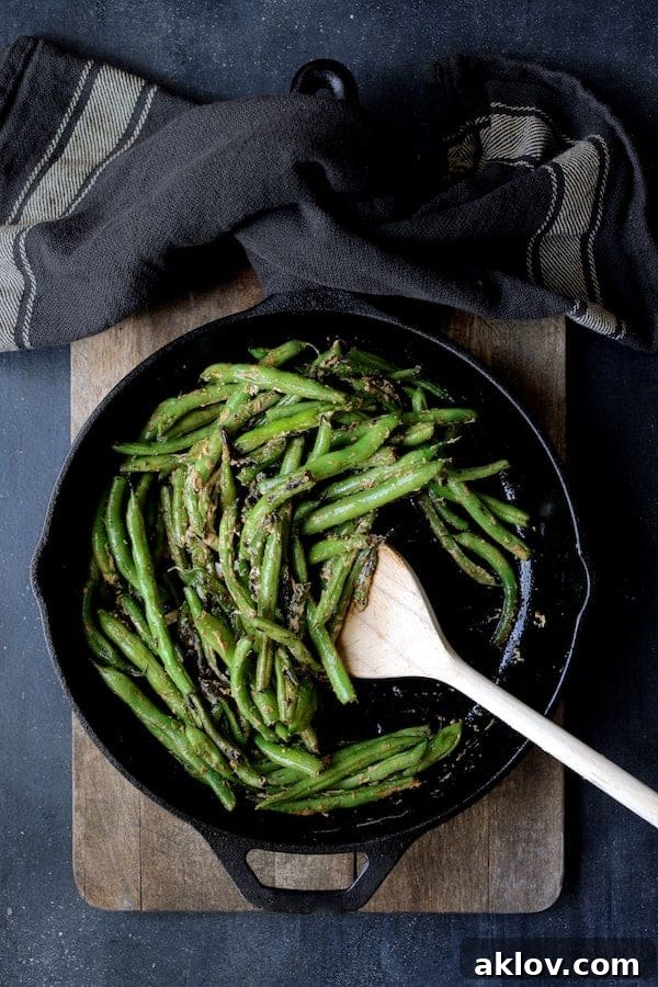 Photo of Skillet Charred Green Beans with Goat Cheese Chipotle Butter in cast iron skillet being stirred with wooden spoon.
