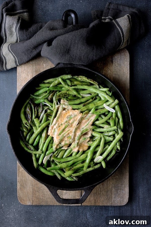 Photo of Skillet Charred Green Beans with Goat Cheese Chipotle Butter in cast iron skillet on wood cutting board.