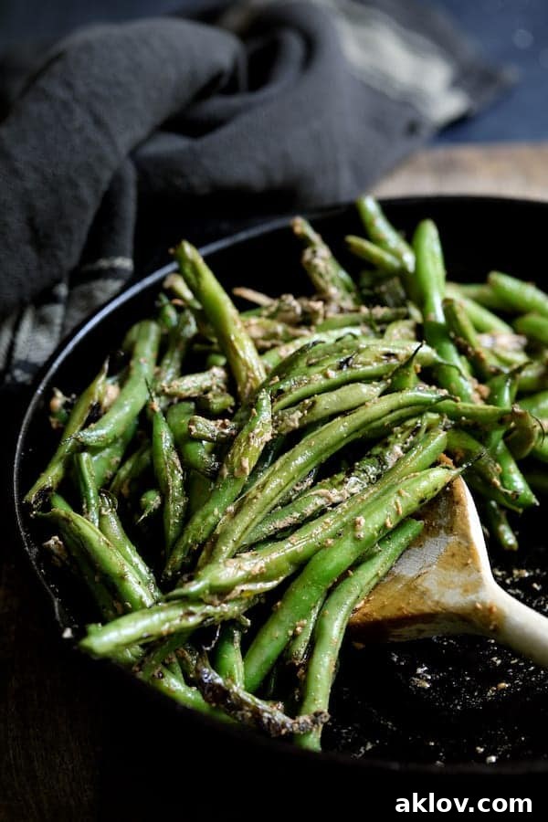 Photo of Skillet Charred Green Beans with Goat Cheese Chipotle Butter in cast iron skillet being stirred with wooden spoon.