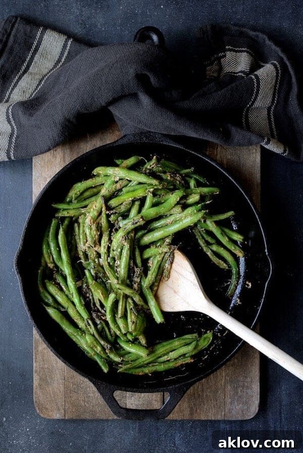 Charred green beans in cast iron skillet being stirred with wooden spoon.