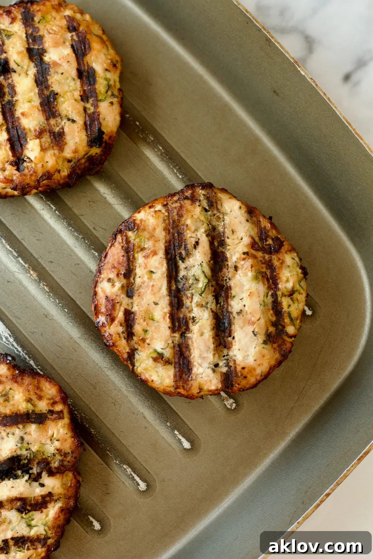 Ground chicken burgers perfectly grilled on a ridged grill pan, showcasing appealing sear marks.