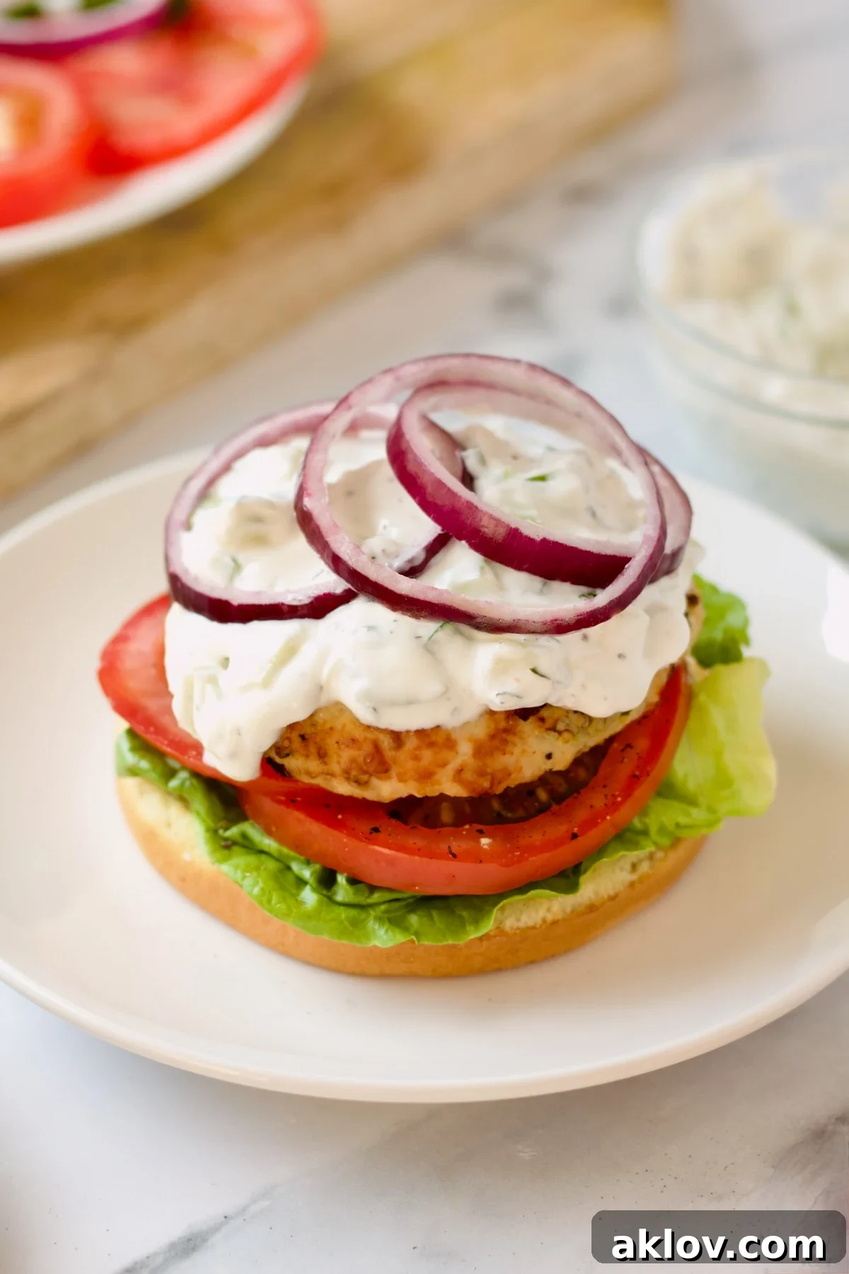 A vibrant Ground Chicken Burger with Spicy Tzatziki, beautifully plated on a white dish, ready for the top bun to complete this gourmet meal.