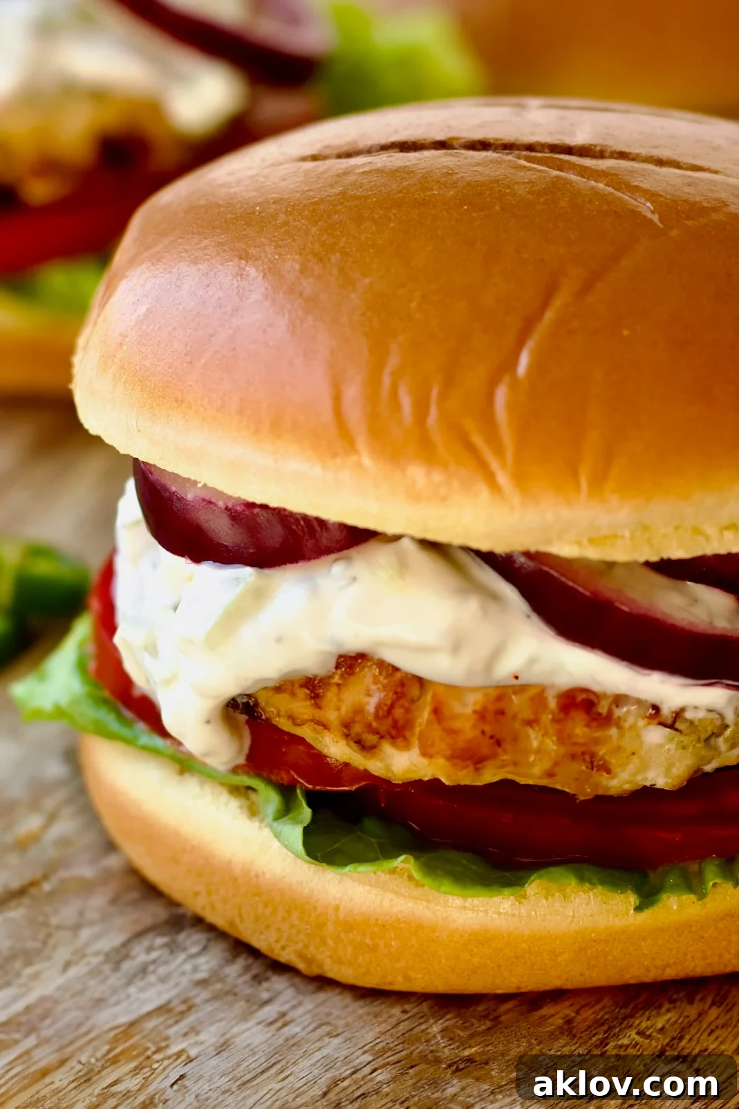 A beautifully assembled Ground Chicken Burger with Spicy Tzatziki resting on a wooden surface, ready to be enjoyed.
