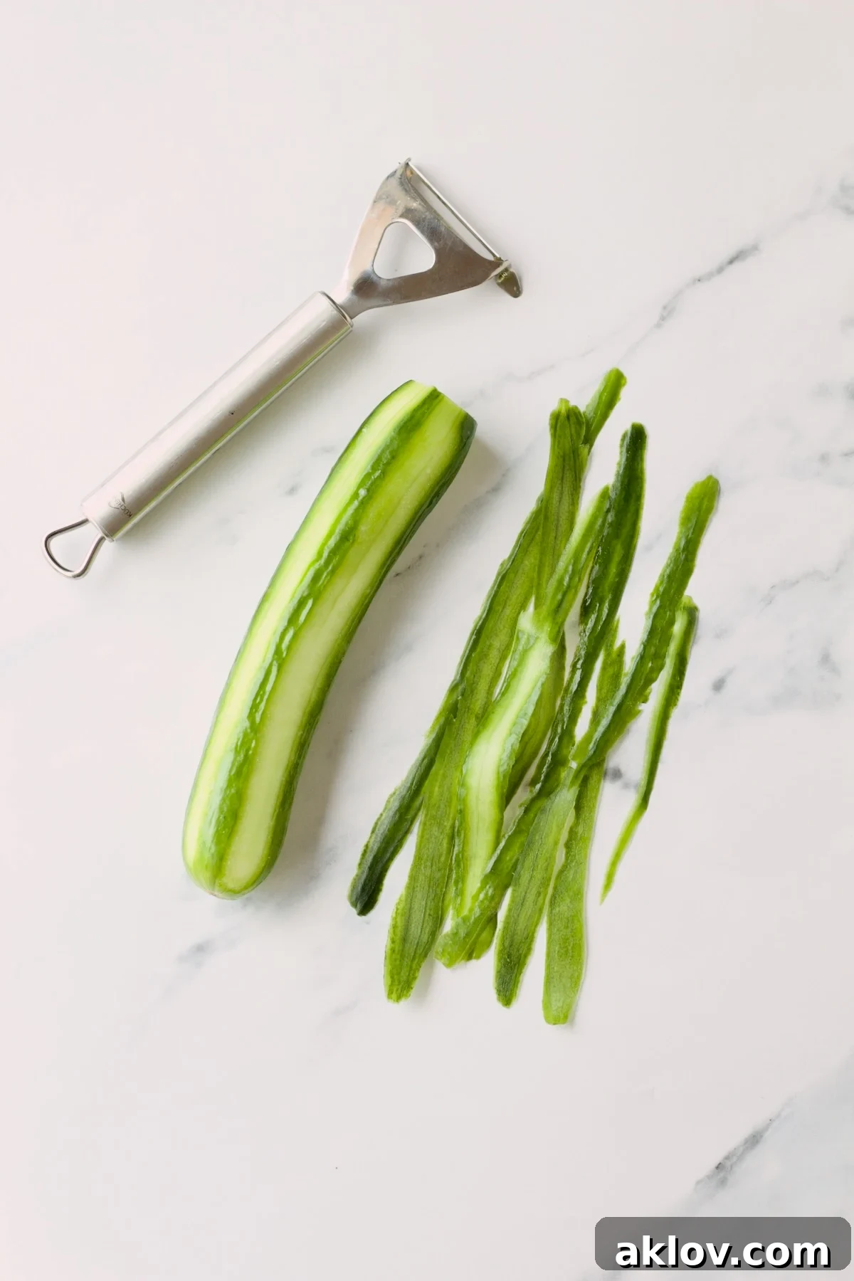 A semi-peeled cucumber rests on a countertop with a vegetable peeler, demonstrating a technique for aesthetic presentation.