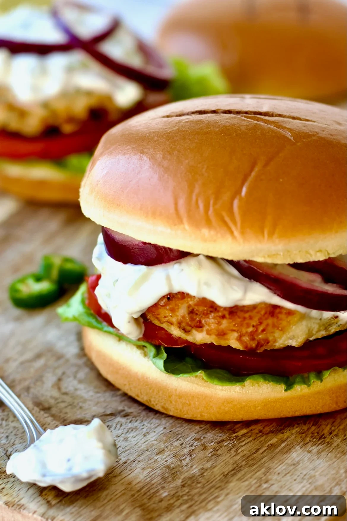 Grilled Ground Chicken Burgers with Spicy Tzatziki sauce presented on a wooden cutting board, accompanied by a spoonful of the creamy sauce.