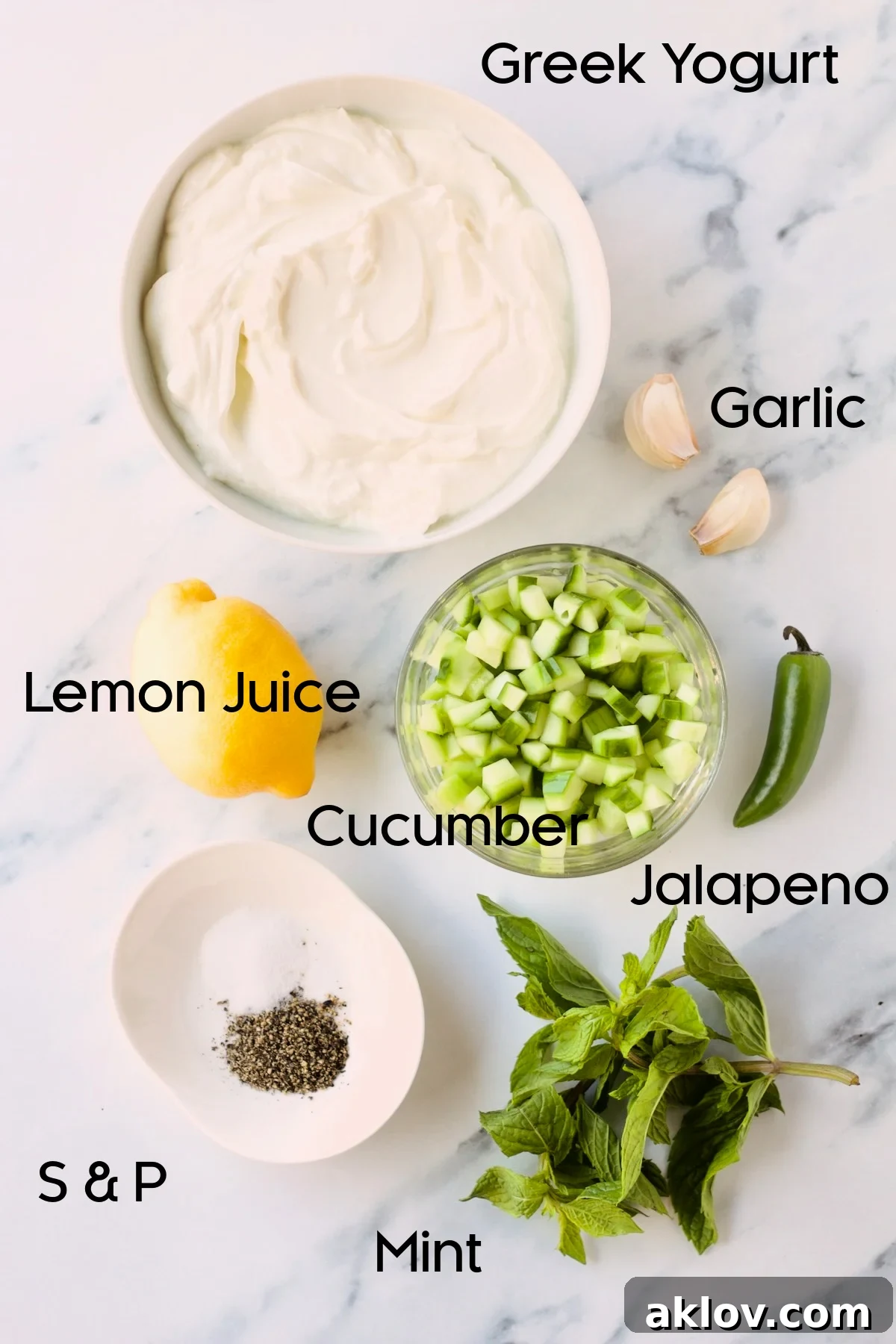 Ingredients for the spicy tzatziki sauce, including cucumber, jalapeno, garlic, mint, and Greek yogurt, displayed in small bowls on a marble countertop.