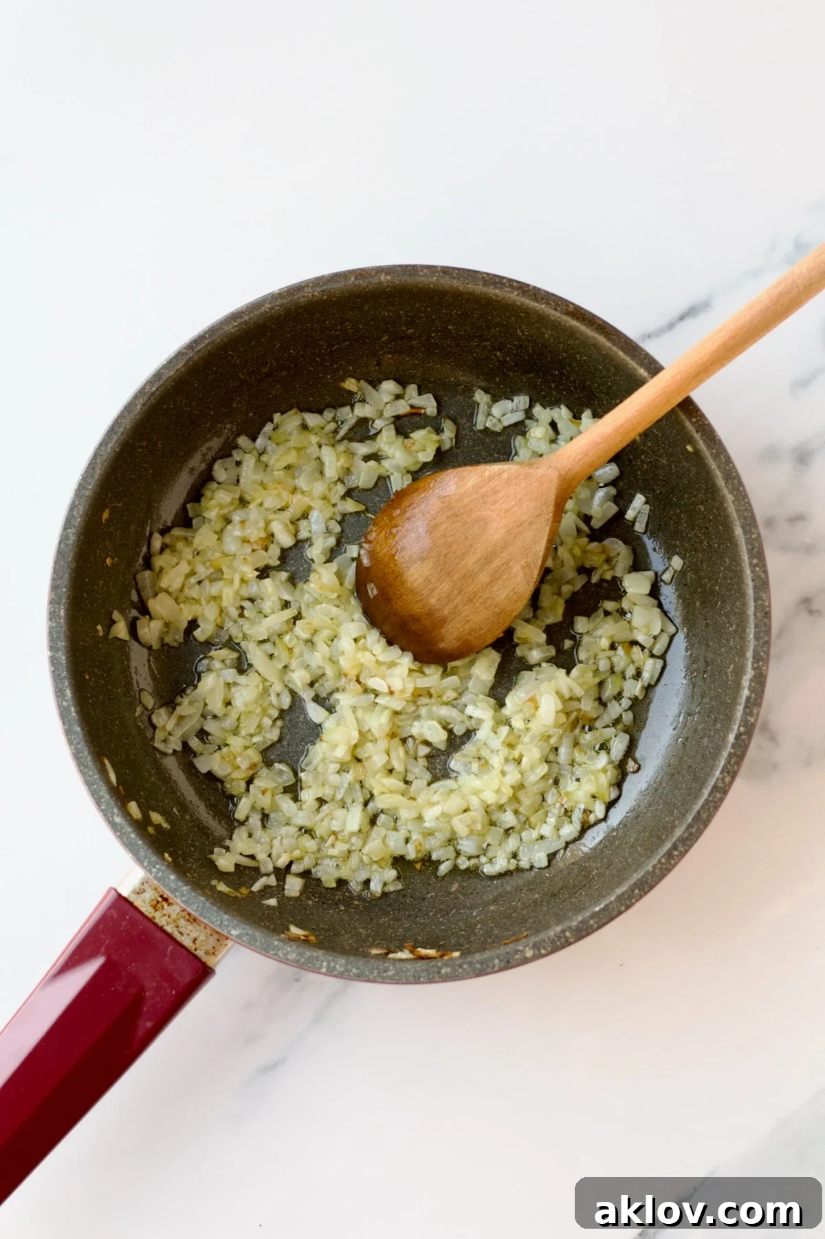 Finely chopped onions are being skillfully sautéed in olive oil within a nonstick skillet, stirred gently with a wooden spoon.