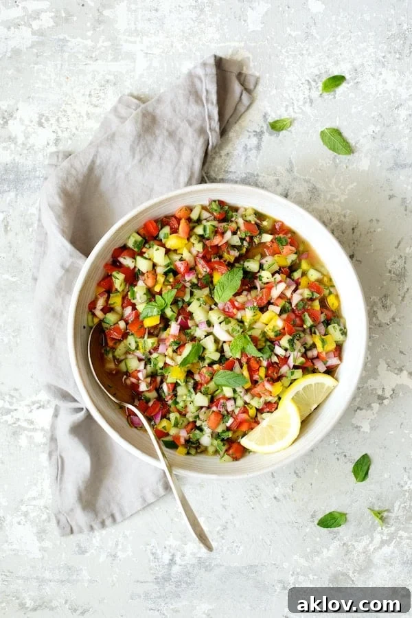 A pristine white serving bowl filled with colorful Middle Eastern Chopped Salad, accented by vibrant lemon slices and set against a sophisticated gray background with a matching napkin.