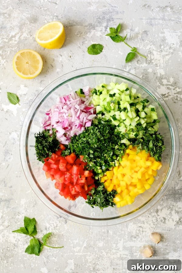 A vibrant collection of fresh, uncooked salad ingredients meticulously chopped and placed in a large glass mixing bowl, ready to be combined.