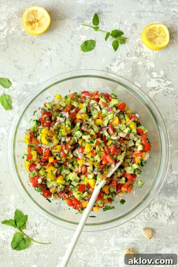 The Middle Eastern Chopped Salad, now perfectly stirred and dressed, showcasing its medley of vibrant vegetables in a glass mixing bowl with a white serving spoon.