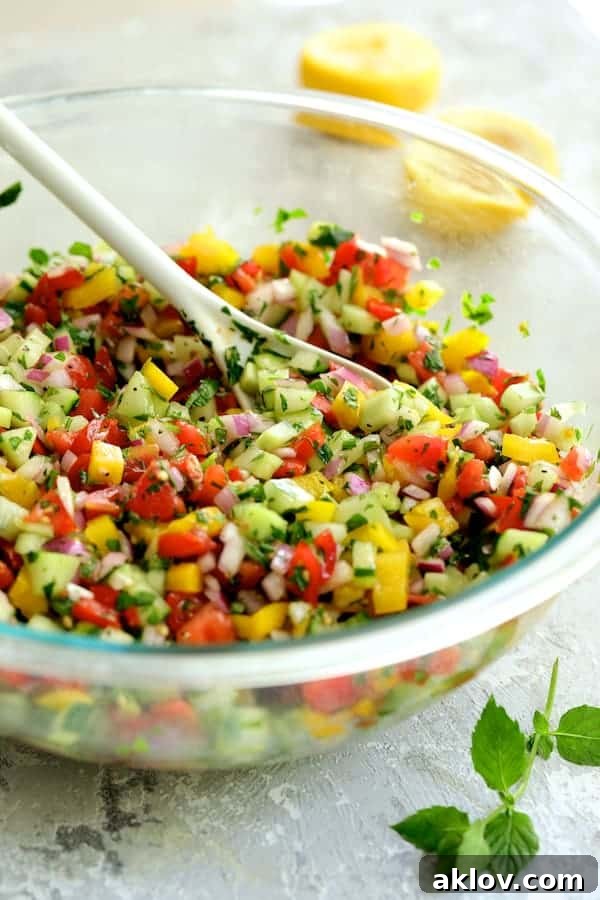 A vibrant Middle Eastern Vegetable Salad, freshly stirred and glistening with its zesty dressing, in a clear glass mixing bowl, ready for serving.