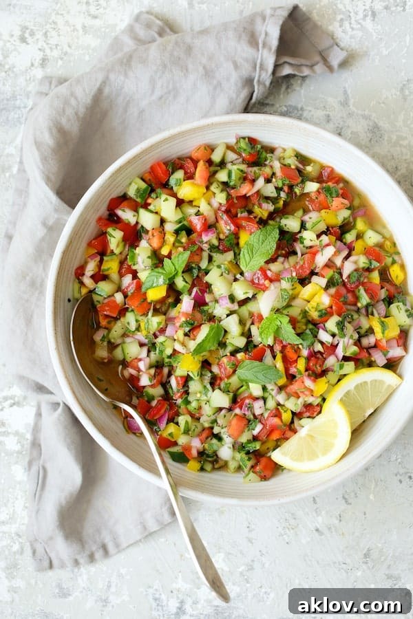 The final presentation of the Middle Eastern Chopped Salad in an elegant white serving bowl, garnished with fresh lemon slices, resting on a gray background with a delicate gray napkin.