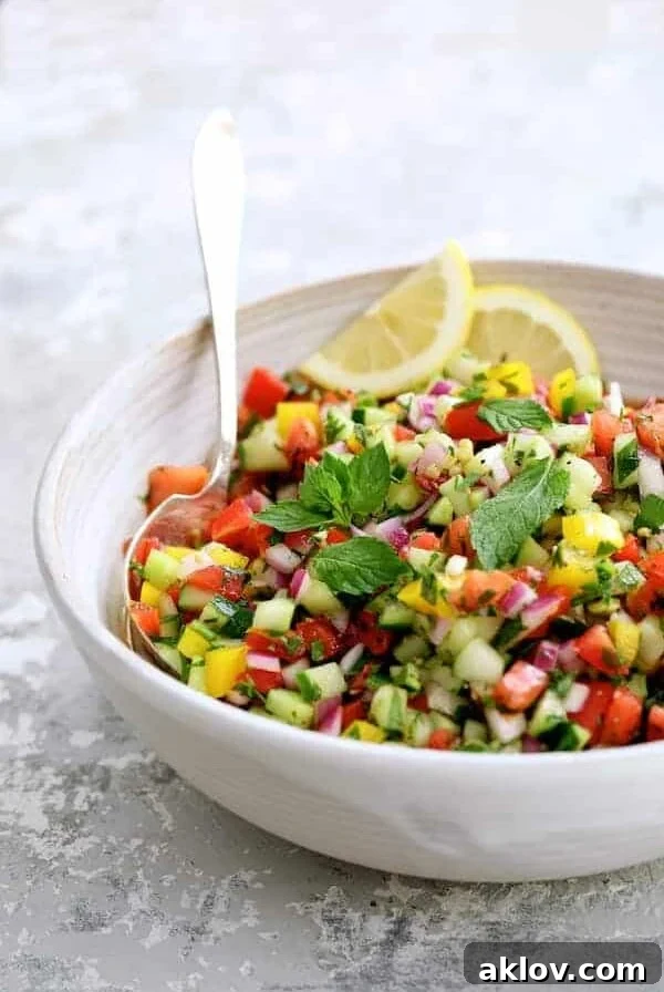 Middle Eastern Chopped Salad in a white serving bowl garnished with mint sprigs and lemon slices.