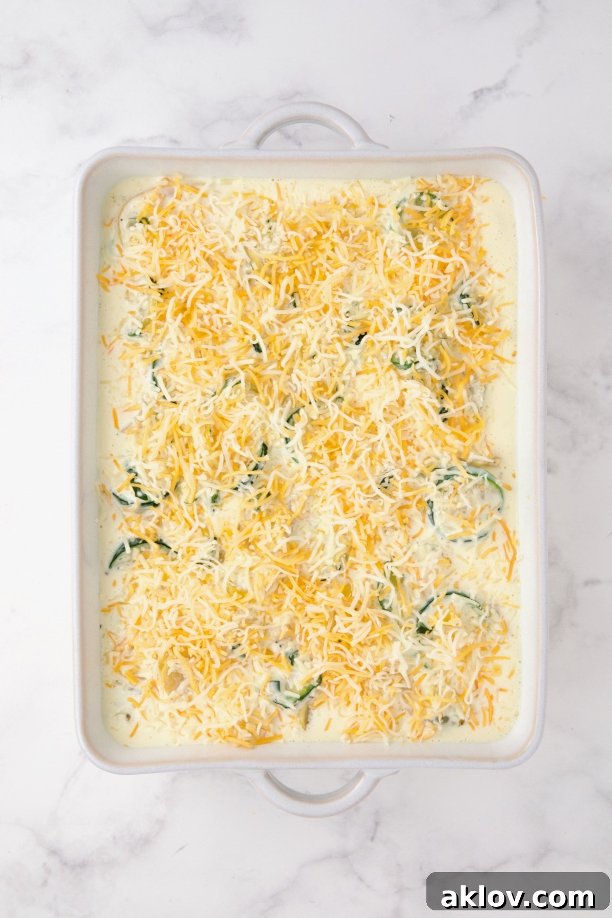 Cooked zucchini, yellow squash, poblano, and corn in a white rectangular baking dish with custard added and the remaining cheese sprinkled over the top.