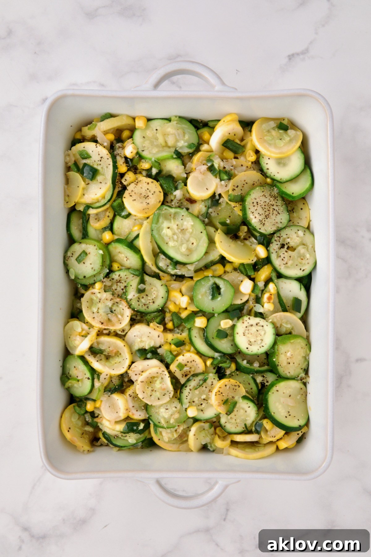 Cooked zucchini, yellow squash, poblano, and corn transferred to a white rectangular baking dish, cooling slightly.