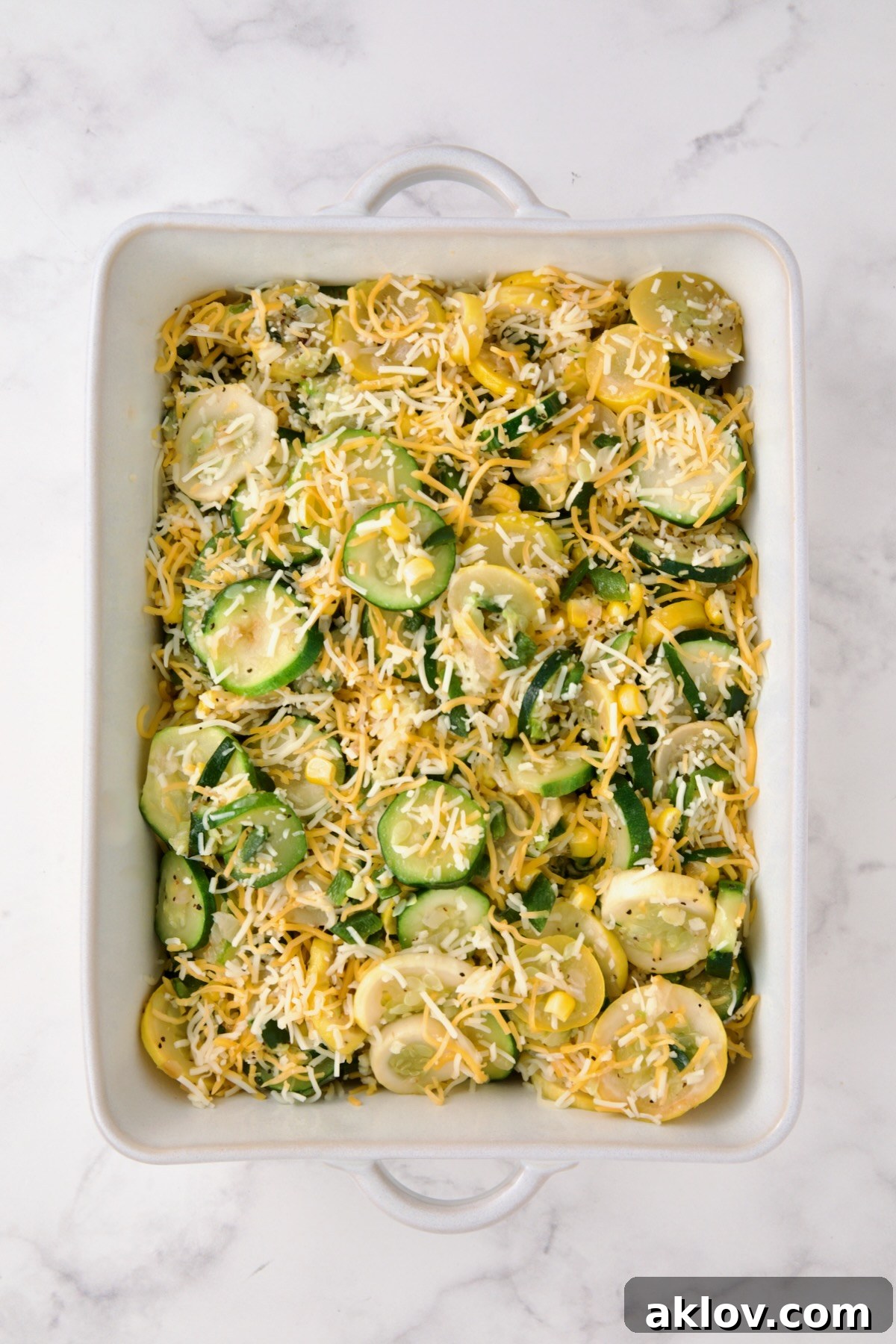 Shredded Mexican blend cheese being stirred into the cooked zucchini, yellow squash, poblano, and corn in the baking dish.